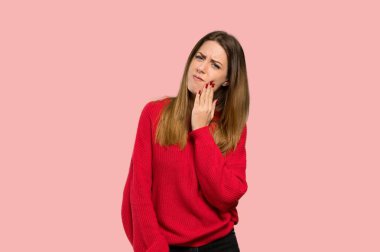 İzole pembe bir arka plan üzerinde diş ağrısı ile kırmızı kazaklı genç kadın