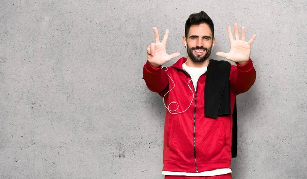 Handsome sportman counting eight with fingers over textured wall