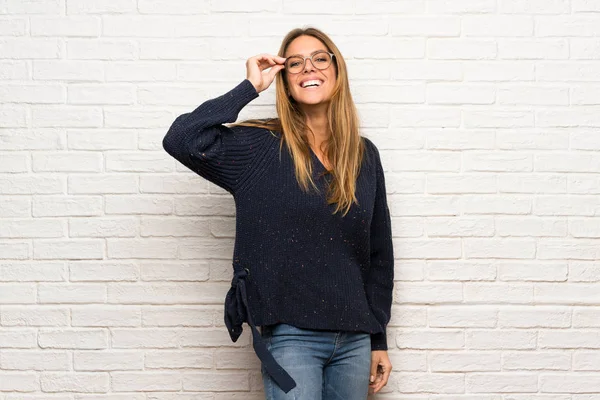 Blonde woman over brick wall with glasses and surprised