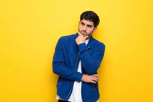 Man with blue jacket over yellow wall thinking