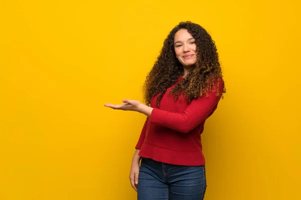 Adolescente Chica Con Suéter Rojo Sobre Pared Amarilla Presentando Una —  Fotos de Stock
