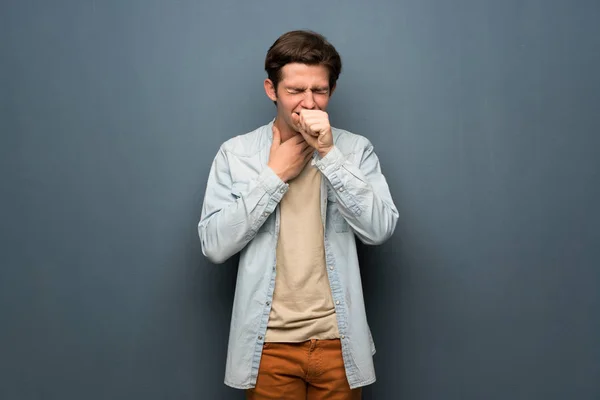 Teenager man with jean jacket over grey wall is suffering with cough and feeling bad