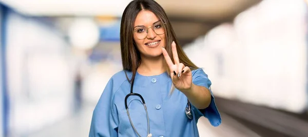 年轻护士微笑着在医院展示胜利的标志 — 图库照片