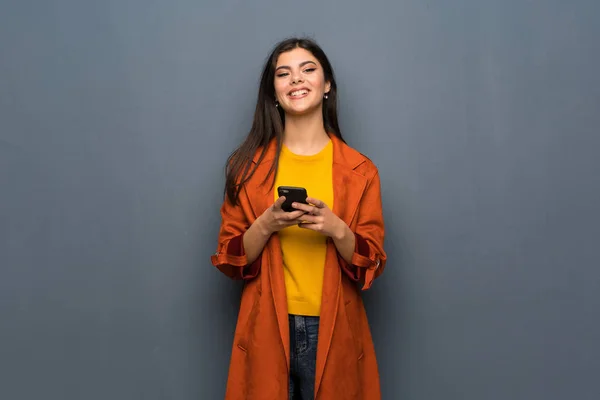 Chica Adolescente Con Abrigo Sobre Pared Gris Enviando Mensaje Con — Foto de Stock