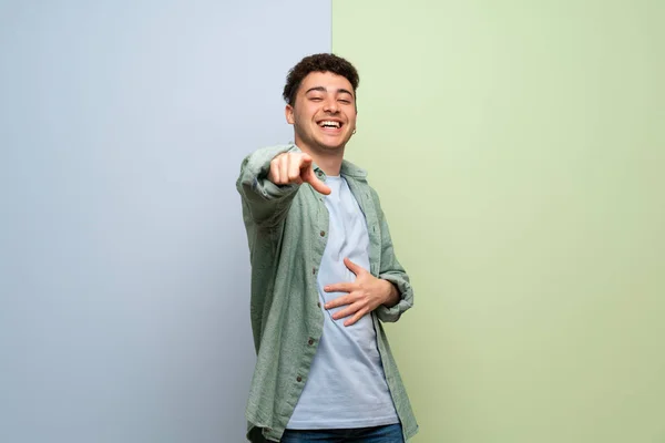 Młody Człowiek Niebieskim Zielonym Tle Wskazując Palcem Kogoś Śmiech — Zdjęcie stockowe