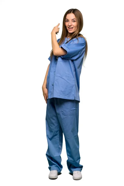 Full body Young nurse pointing back with the index finger on isolated background