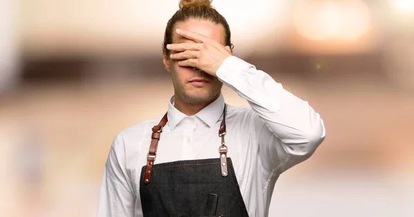 Barber man in an apron covering eyes by hands. Do not want to see something in a barber shop
