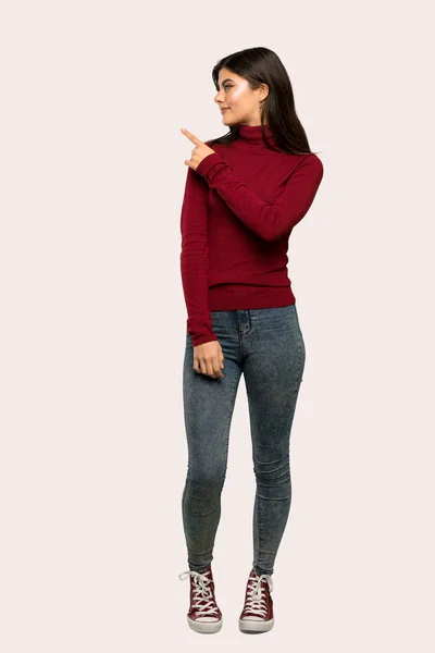 一个有高领毛衣的少年女孩的全长照片 她的背景是指向孤立的背景 — 图库照片