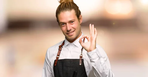 Barber man in an apron showing an ok sign with fingers in a barber shop