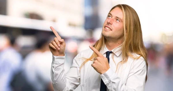 人差し指で指していると屋外で見上げると長い髪のブロンドの実業家 — ストック写真