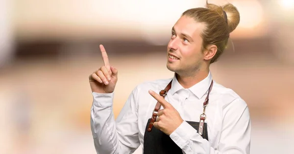 Barber man in an apron pointing with the index finger and looking up in a barber shop