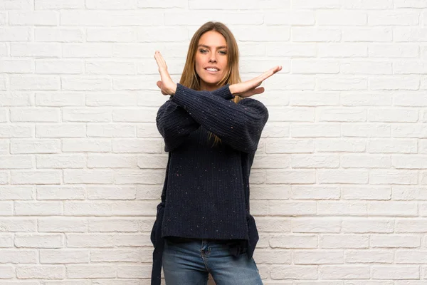 Blonde woman over brick wall making NO gesture