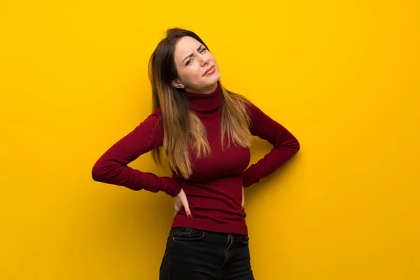Woman with turtleneck over yellow wall suffering from backache for having made an effort