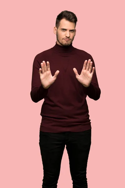 Man with turtleneck sweater making stop gesture and disappointed over pink background