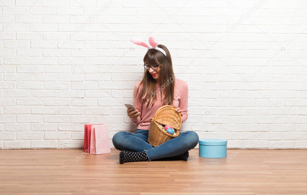 Woman with bunny ears for Easter holidays sitting on the floor sending a message or email with the mobile