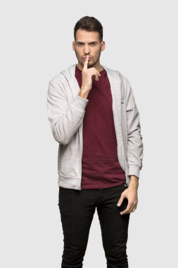 Adam bir işaret parmağını ağzına gri arka plan üzerinde koyarak sessizlik jest gösteren kazak ile