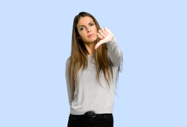 başparmak aşağı işareti negatif ifade ile mavi arka plan üzerinde gösterilen genç kız