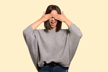 Genç kadın gözleri eller tarafından kapsayan. Ne ileri izole sarı arka plan üzerinde olduğunu görmek için sürpriz