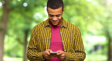 Genç afro Amerikalı adam parkta mobil ileti gönderme