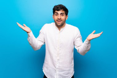 Sürpriz ve şok yüz ifadesi ile izole mavi duvarın üzerinden genç adam