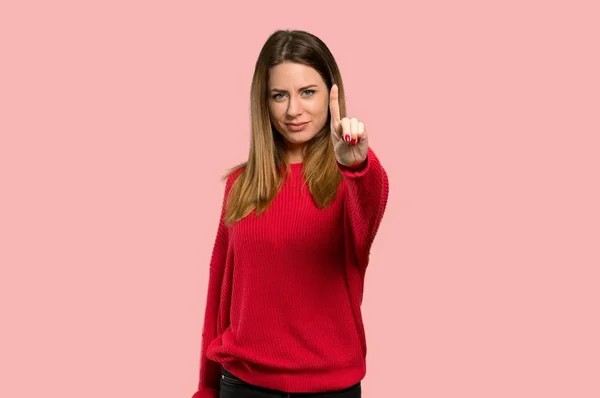 年轻的妇女与红色毛衣显示和举起手指在被隔绝的粉红色背景 — 图库照片