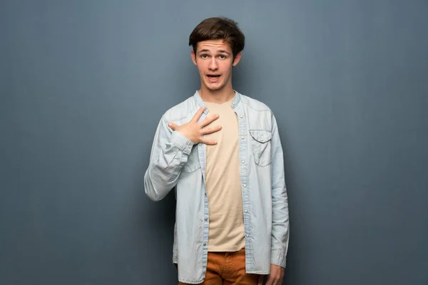 Teenager man with jean jacket over grey wall surprised and shocked while looking right