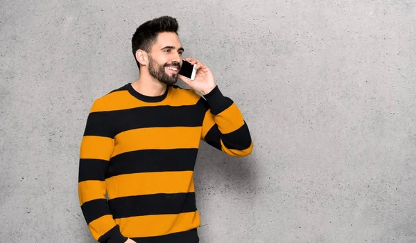 Handsome man with striped sweater keeping a conversation with the mobile phone over textured wall