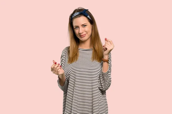 Young woman with headscarf making money gesture over isolated pink background