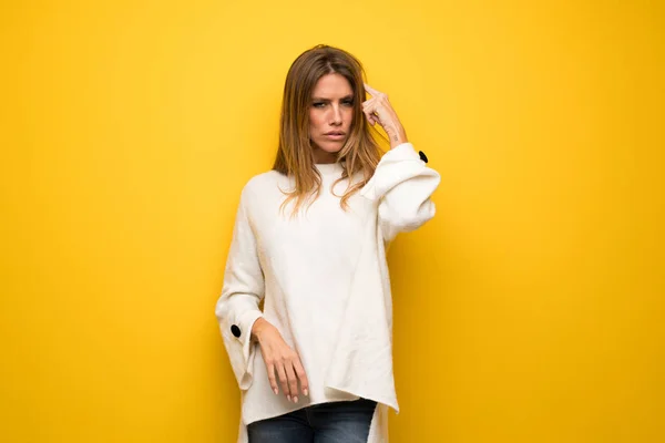 Blonde woman over yellow wall making the gesture of madness putting finger on the head