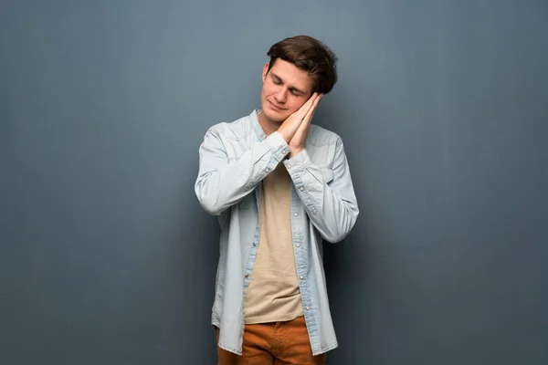 Teenager man with jean jacket over grey wall making sleep gesture in dorable expression