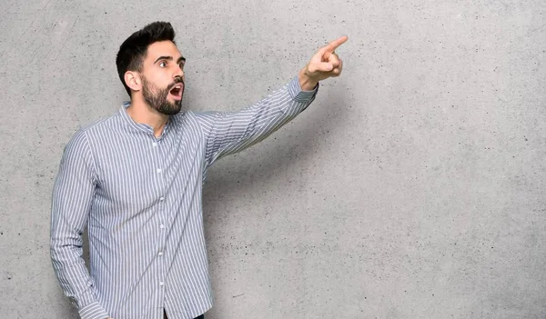 Elegant man with shirt pointing away over textured wall