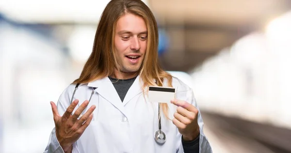 Doctor man holding a credit card and surprised in a hospital