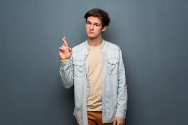 Jean ceket gri duvar ile en iyi dilek ve geçiş parmak üzerinde olan genç adam