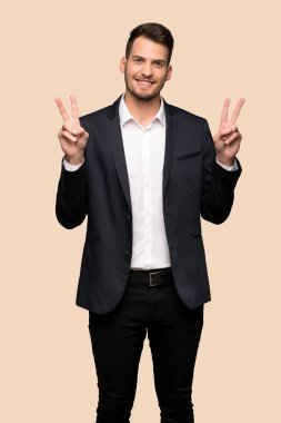 Gülümseyen ve her iki el ile zafer işareti koyu sarı arka plan üzerinde gösterilen yakışıklı iş adamı