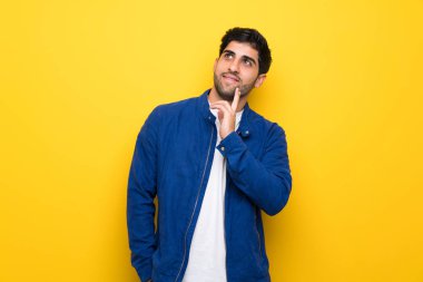 Mavi ceket ve sarı duvar ararken bir fikir düşünce üzerinde olan adam