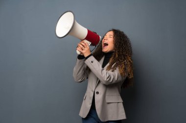 Teenager girl over blue wall shouting through a megaphone clipart