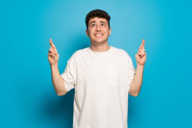 En iyi dilek ve geçiş parmakları ile mavi arka plan üzerinde genç adam