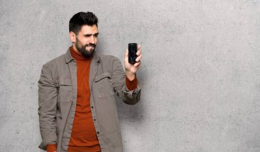 Kırık smartphone dokulu duvar'ın üstüne holding ile sakallı yakışıklı adam sorunlu