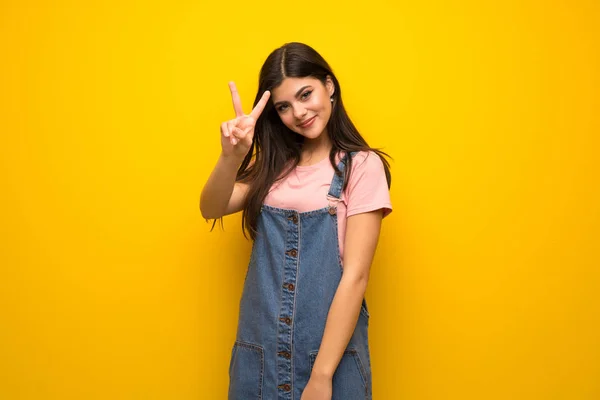 Teenagermädchen Über Gelbe Wand Lächelt Und Zeigt Siegeszeichen — Stockfoto