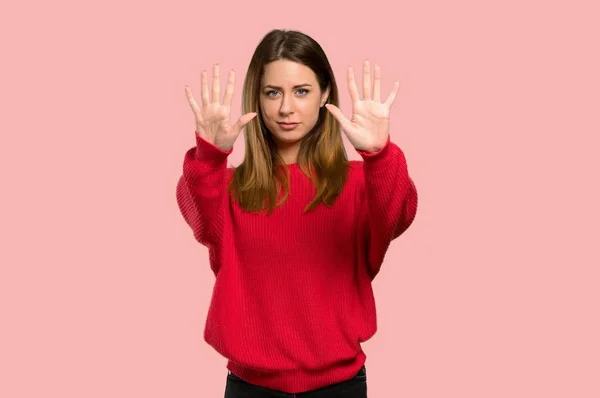 分離のピンクの背景に指で を数えて赤いセーターを持つ若い女性 — ストック写真
