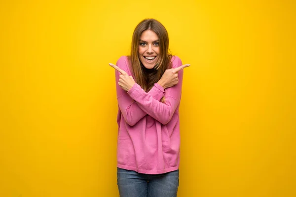 疑問を持つ根を指している黄色の壁にピンクのセーターの女性 — ストック写真
