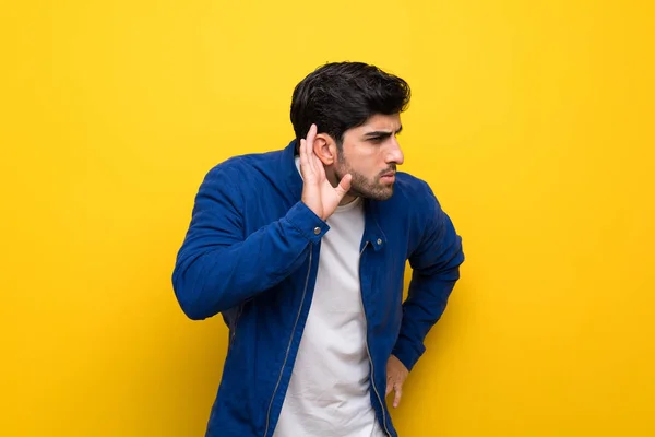 Człowiek Niebieską Kurtkę Żółty Ścianę Słuchając Coś Kładąc Rękę Ucho — Zdjęcie stockowe