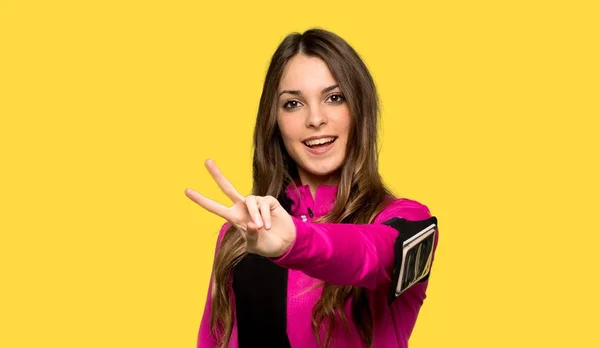 Junge Sportlerin Lächelt Und Zeigt Siegeszeichen Vor Isoliertem Gelben Hintergrund — Stockfoto