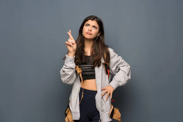 Teenager traveler girl over wall with fingers crossing and wishing the best