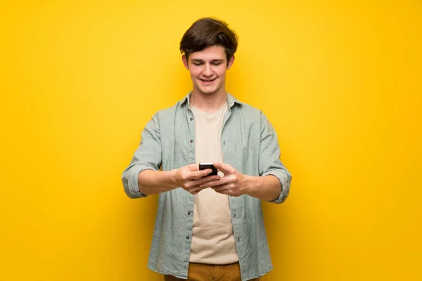 Jugendlicher Mann Über Gelbe Wand Und Sendet Nachricht Mit Handy — Stockfoto