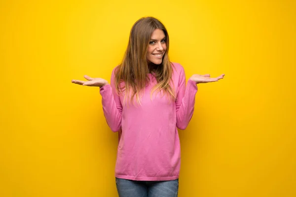 手を上げながら疑問を持つ黄色の壁にピンクのセーターの女性 — ストック写真