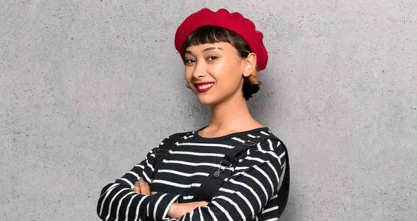 Young woman with beret with arms crossed and looking forward over textured wall