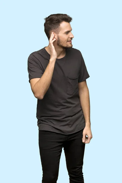 Man Black Shirt Listening Something Putting Hand Ear Blue Background — Stock Photo, Image