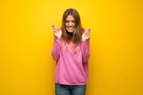 妇女与粉红色的毛衣在黄色的墙壁与手指交叉 并祝愿最好的 — 图库照片