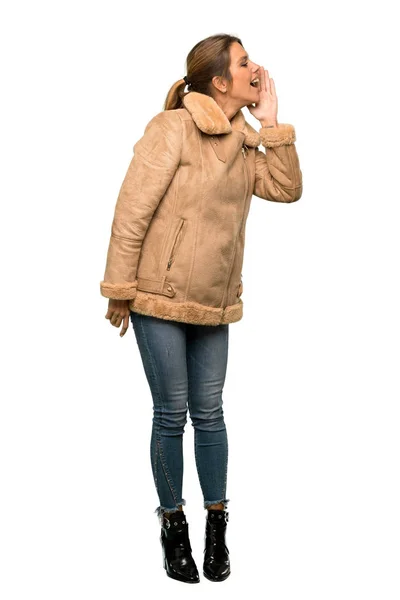 分離の白い背景の上で口を横に大きく開いて叫びコートと金髪女性のフルレングス ショット — ストック写真